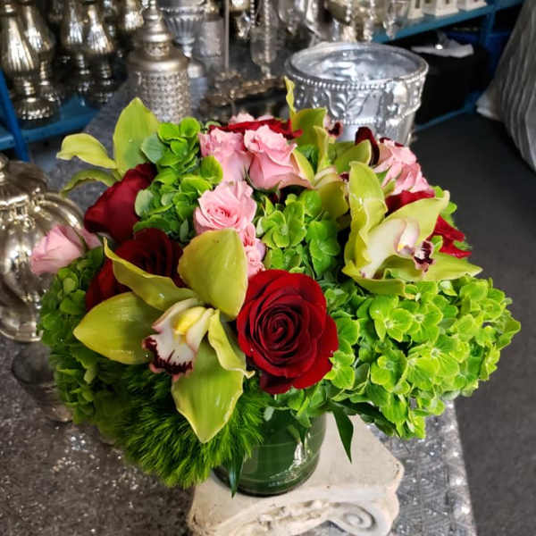 Bouquet of red roses, pink blooms, and green orchids in a glass vase