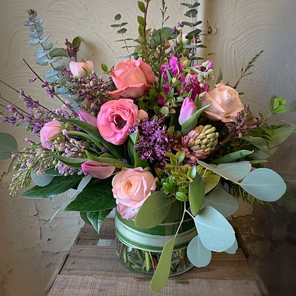Pink and peach roses with purple blooms in a glass vase