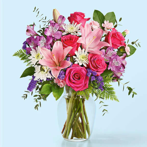Bouquet of pink roses, lilies, and purple flowers in a clear glass vase