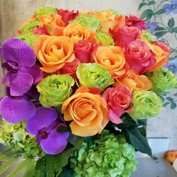 Bouquet of orange and pink roses with purple orchids in a glass vase