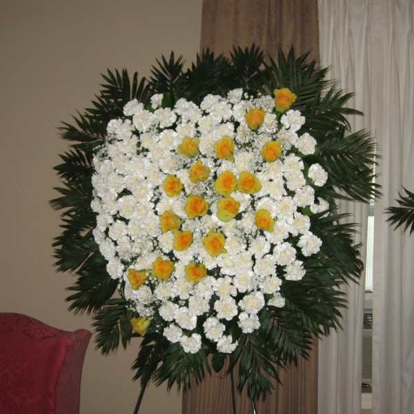 Standing floral spray of white and yellow flowers on a dark green frame