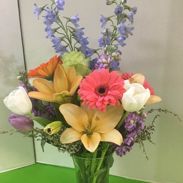 Mixed bouquet in a clear glass vase with lilies, gerbera daisies, and tulips