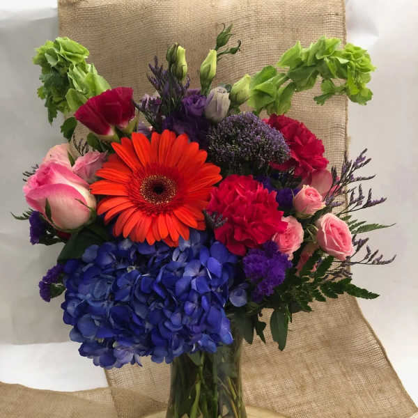 Colorful mixed bouquet in a glass vase with hydrangeas, roses, and a gerbera daisy