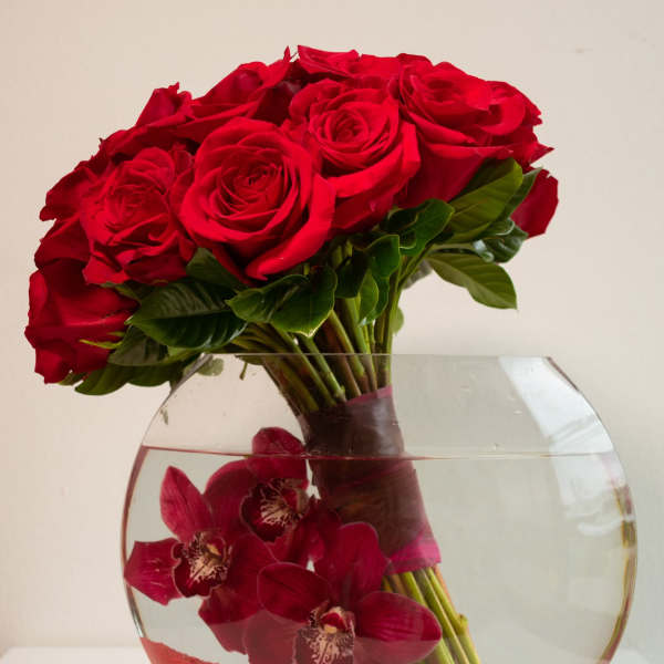Red roses and dark red orchids arranged in a round glass vase