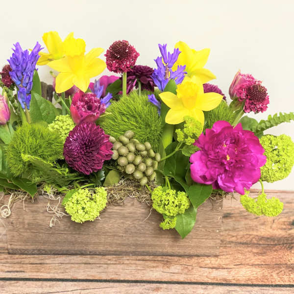 Bright mixed flower arrangement in a wooden box with yellow and purple blooms