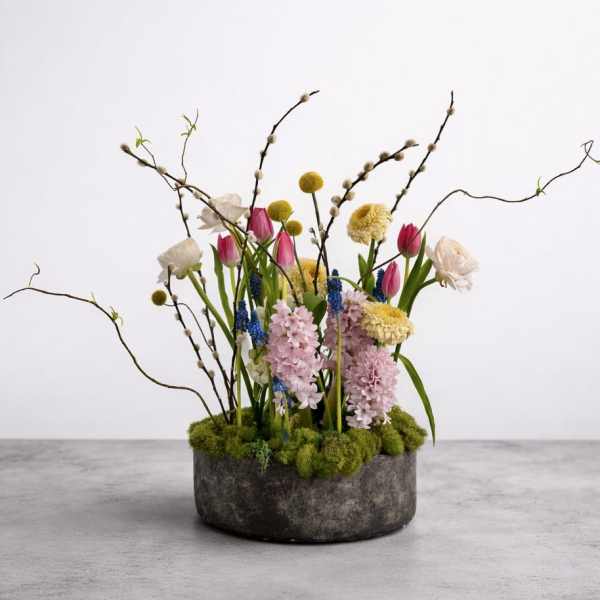 Mixed floral arrangement in a round gray container with tall branches