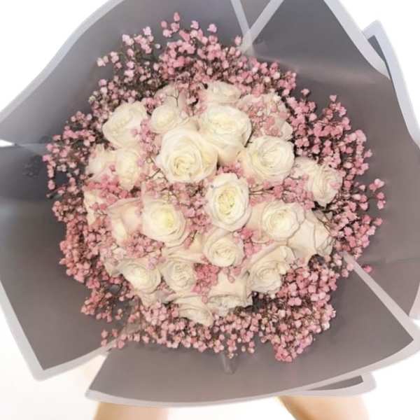 Bouquet of white roses with pink filler flowers in gray wrapping