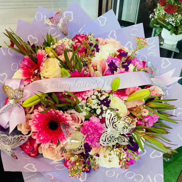 Large bouquet of pink, white, and peach flowers wrapped in lavender paper