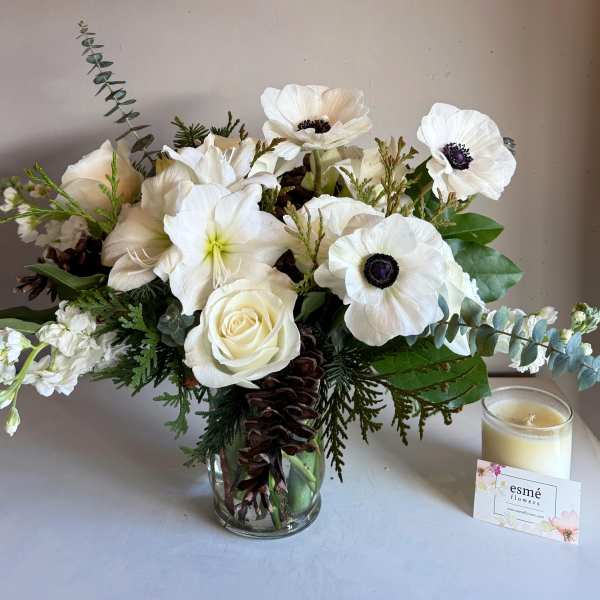 White floral arrangement in a glass vase with a candle beside it
