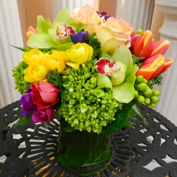 Colorful mixed bouquet in a dark glass vase with tulips, roses, and orchids