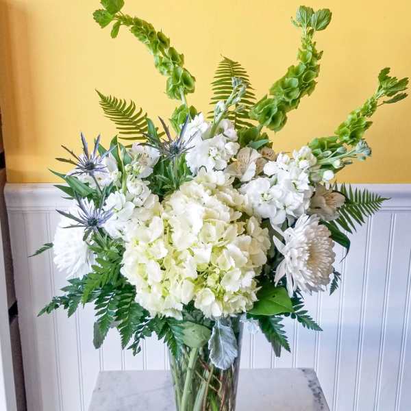 White floral arrangement in a clear glass vase with tall green spikes