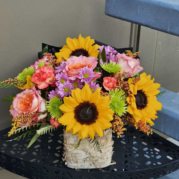 Bouquet of sunflowers, pink roses, and purple daisies in a birch container