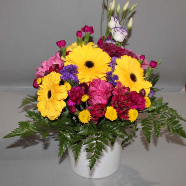 Bright mixed flower arrangement in a white pot with yellow daisies and pink blooms