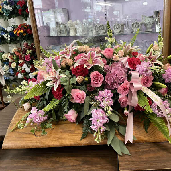 Large pink floral spray with lilies, roses, and ribbon on a wooden table