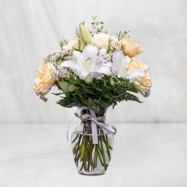 Bouquet of white lilies and pale peach roses in a glass vase