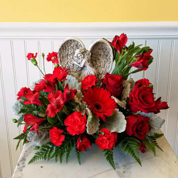 Red floral arrangement with roses, gerbera daisies, and carnations around an angel wing ornament