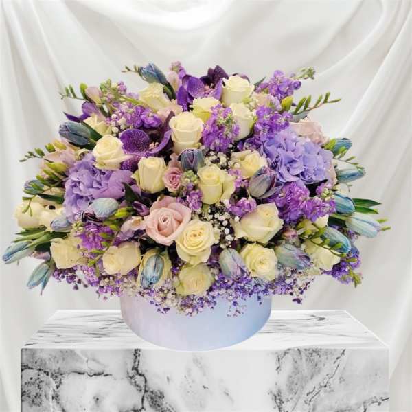 Lavender and cream rose bouquet with purple blooms in a white round box