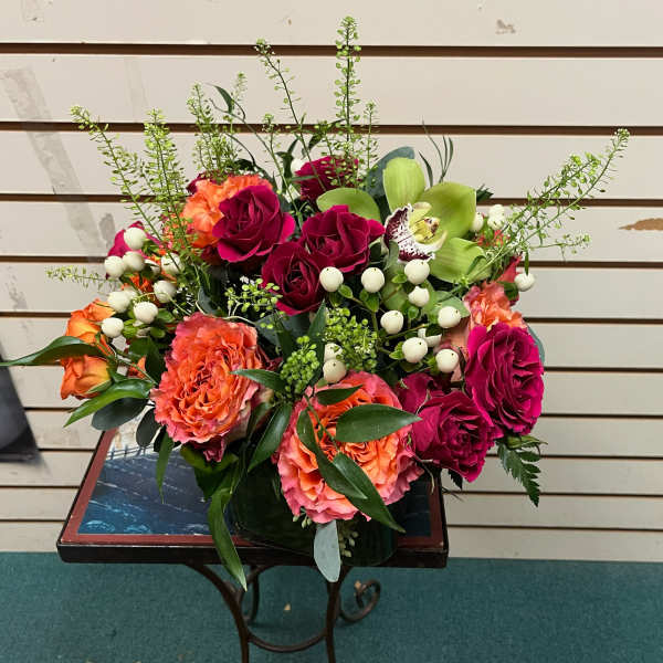 Bouquet of pink and orange roses with green orchids in a vase