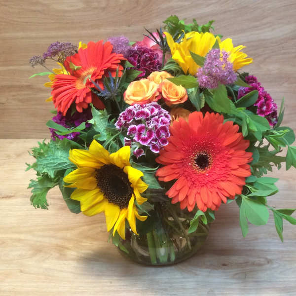 Mixed bouquet with sunflowers, gerbera daisies, roses, and carnations in a glass vase