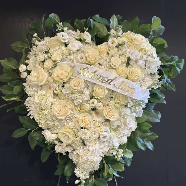 Heart-shaped white floral wreath with a ribbon reading "Beloved Mom"