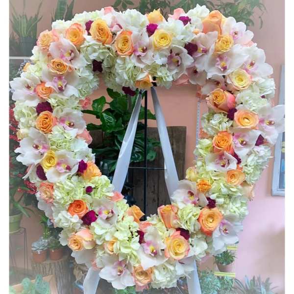 Heart-shaped floral wreath with white orchids, peach roses, and pale hydrangeas