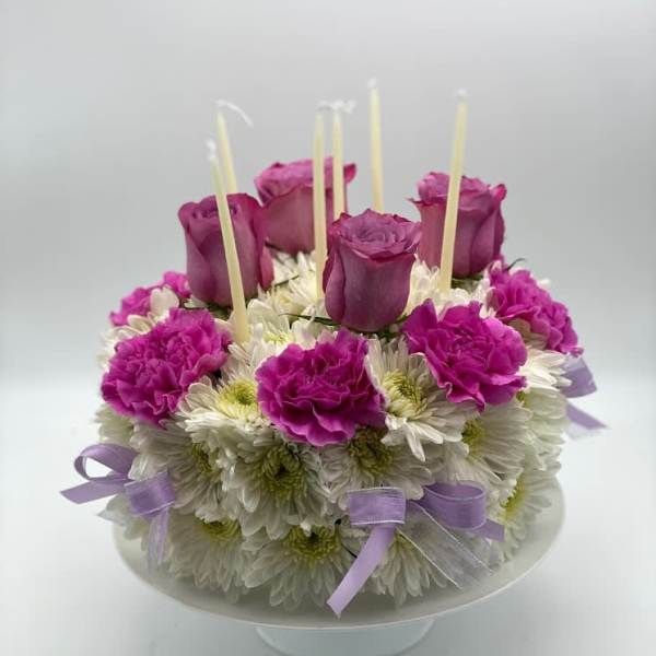 Round floral cake with purple roses and white daisies on a pedestal stand