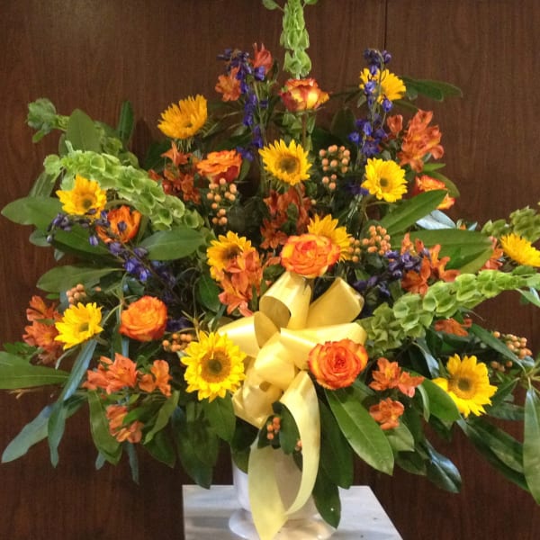 Large mixed bouquet with yellow sunflowers, orange roses, and a yellow ribbon in a vase