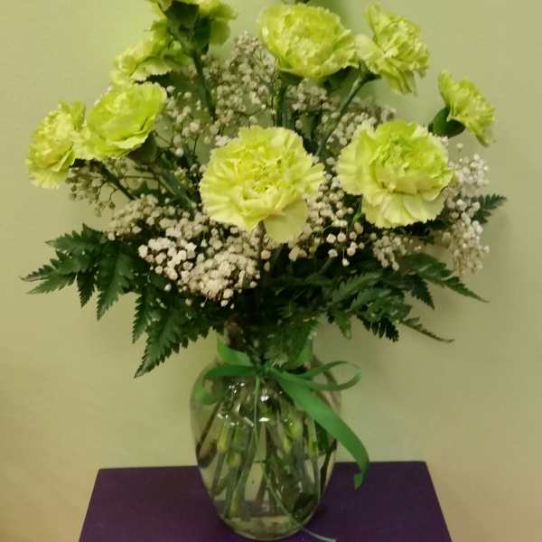 Green carnations and baby's breath in a glass vase with a ribbon