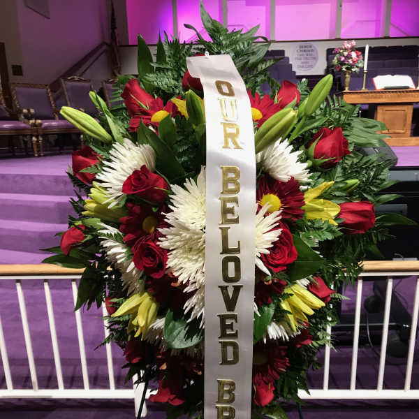 Large funeral wreath of red, white, and yellow flowers with a memorial ribbon
