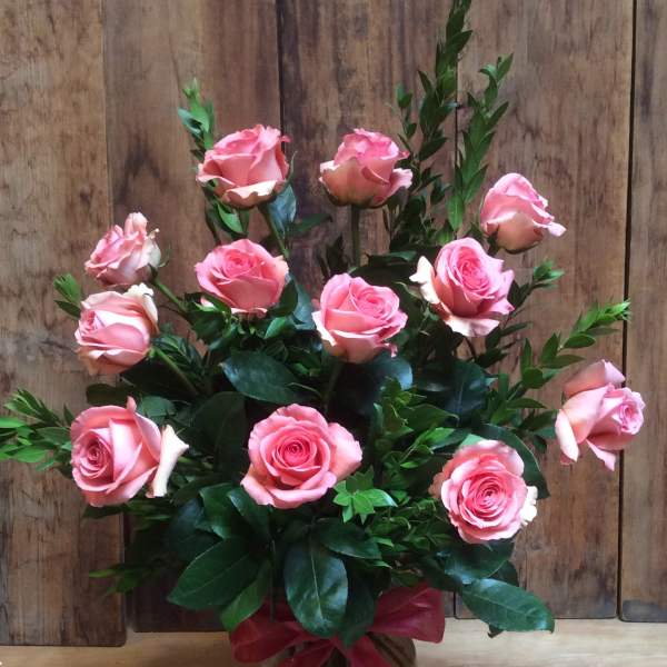 Pink roses arranged in a glass vase with a pink ribbon