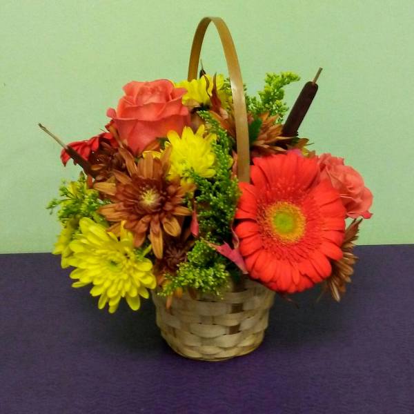 Basket arrangement with pink roses, yellow and orange daisies, and greenery