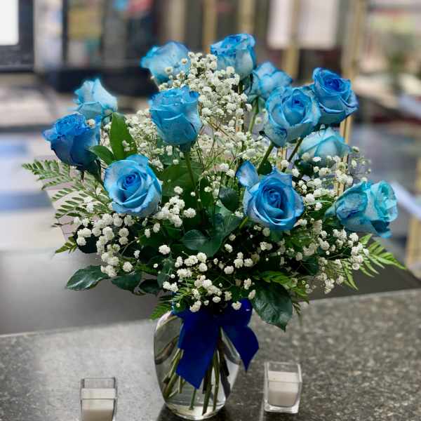 Blue roses in a glass vase with baby's breath and a blue ribbon