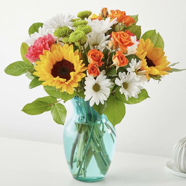 Mixed bouquet of sunflowers, roses, and daisies in a blue glass vase