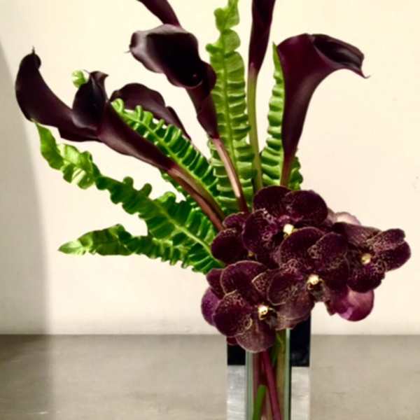 Tall arrangement of dark calla lilies and purple orchids in a glass vase