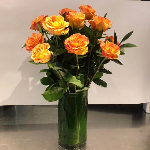 Orange-yellow roses in a tall green glass vase
