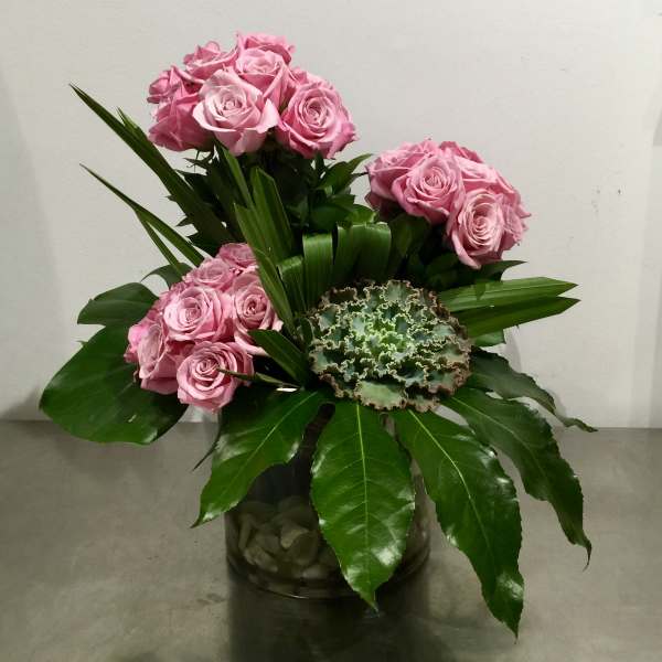 Pink roses arranged in a glass vase with broad green leaves