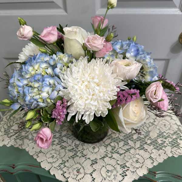 Pastel bouquet with blue hydrangeas, white chrysanthemum, and pink roses in a glass vase.