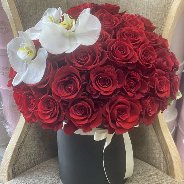 Red roses in a black hat box with white orchids and ribbon