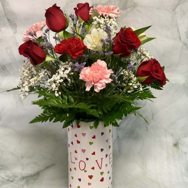 Bouquet of red roses and pink carnations in a heart-patterned vase