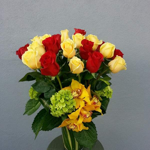 Bouquet of red and yellow roses with yellow orchids in a glass vase