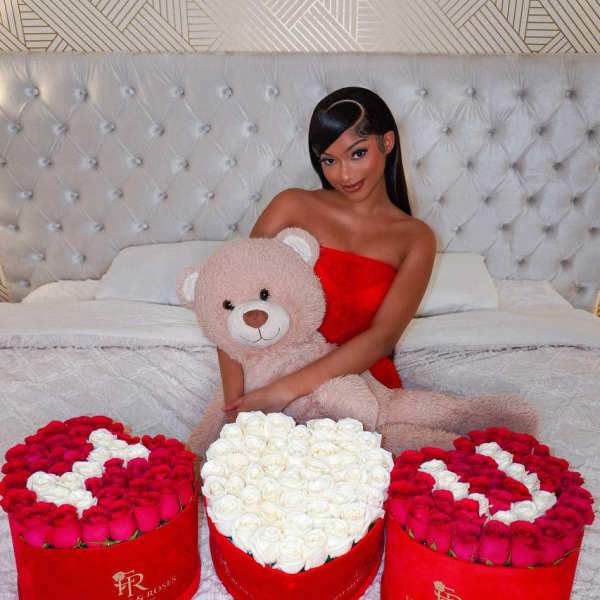 Woman holding a teddy bear with three heart-shaped rose boxes on a bed