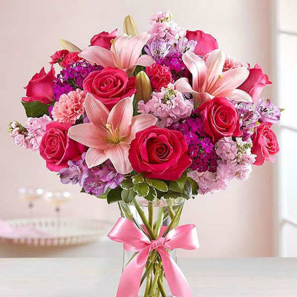 Pink roses and lilies arranged in a glass vase with a pink ribbon