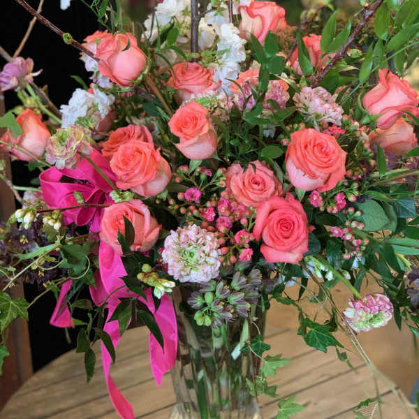 Pink roses and mixed blooms arranged in a clear glass vase with ribbon