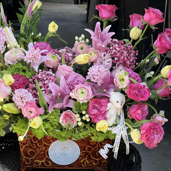 Large pink and yellow floral arrangement in a decorative wooden container