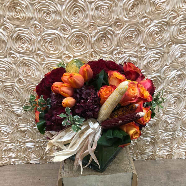 Bouquet of orange and burgundy flowers with decorative corn in a square box