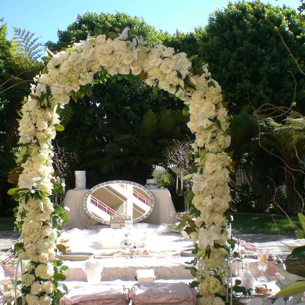 White floral arch over an outdoor ceremony table with candles and a mirror