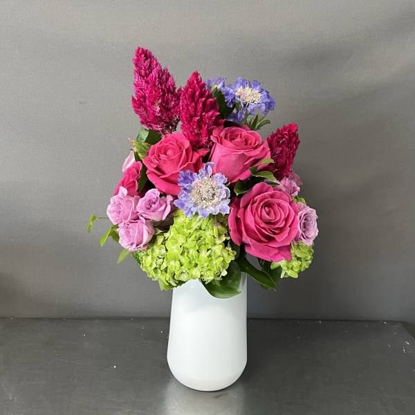 Bright pink roses and purple flowers arranged in a white vase