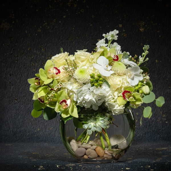 White and pale green floral arrangement in a round glass vase with stones