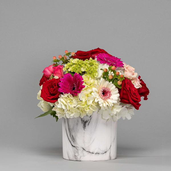 Mixed bouquet of red roses, pink gerberas, and white hydrangeas in a marble vase