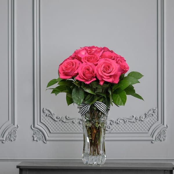 Pink roses arranged in a clear glass vase with a striped ribbon